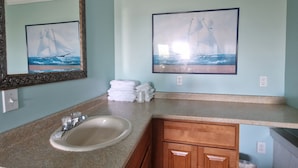 A bathroom with a sink, mirror, and two framed pictures of sailboats.