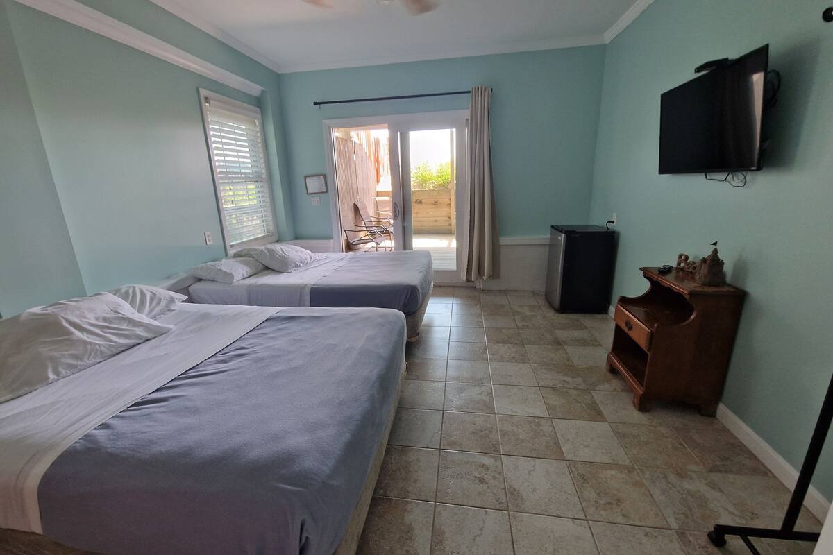 A hotel room with two beds, a ceiling fan, a TV, and a view of the outside.