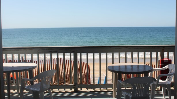 A beachside patio with tables and chairs, overlooking the ocean.