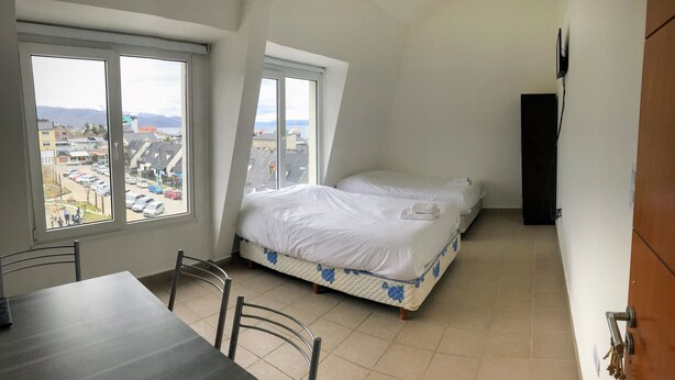 Ein kleiner, sauberer Raum mit zwei Betten, einem Esstisch und Blick auf die Stadt durch große Fenster.