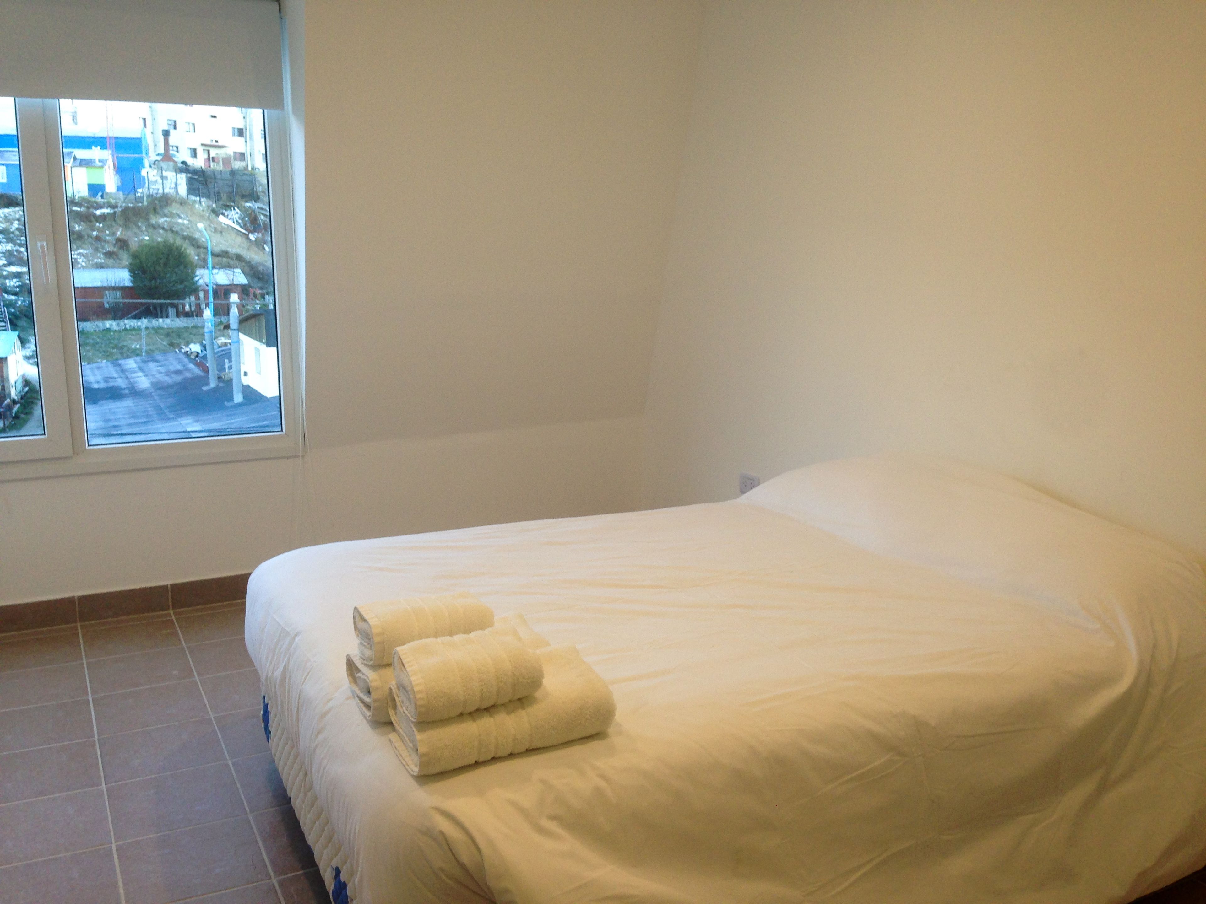Habitación de hotel con una cama grande, una ventana con vistas a edificios y suelo de baldosas.