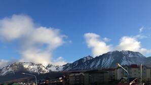 Eine Berglandschaft mit schneebedeckten Gipfeln und blauem Himmel. Im Vordergrund stehen Gebäude mit roten Dächern.
