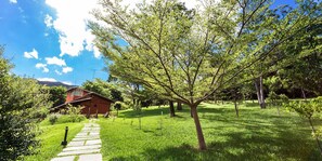 A red wooden house with a stone pathway leading to it, surrounded by lush green grass and trees. - Rancho Cipo Pousada (Santana do Riacho)