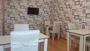 A dining area with a patterned wallpaper, a flat-screen TV, and white chairs with bows. - Kriyus (Gabala)