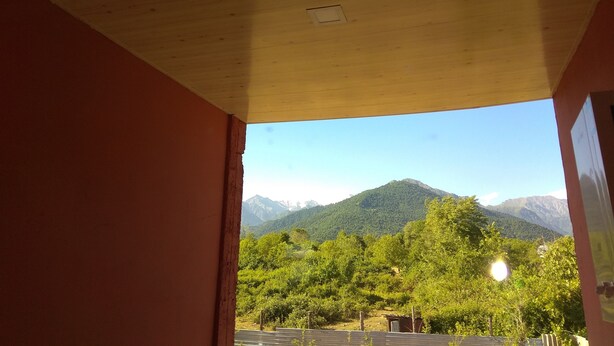 A view through a doorway to a room with a wooden ceiling and a mountain landscape in the background. - Kriyus (Gabala)