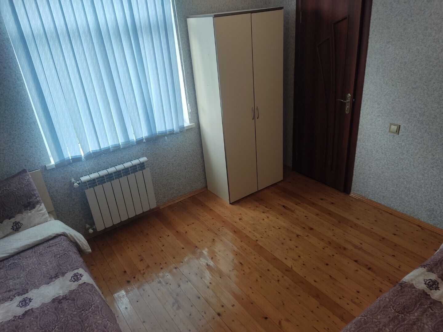 A room with wooden flooring, a radiator, a wardrobe, and a door.