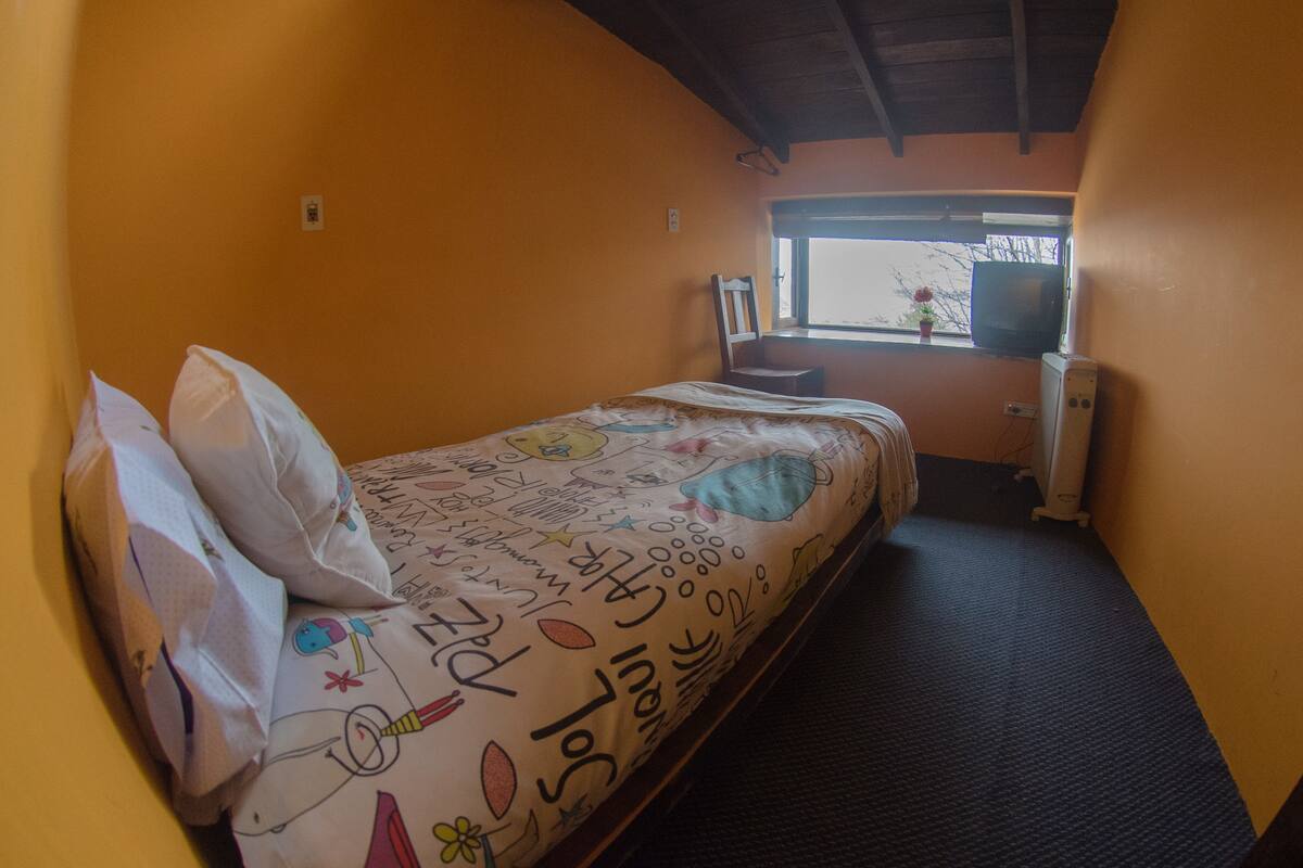 Une petite pièce agréable, dotée d’un lit simple, d’une chaise, d’une fenêtre et d’un radiateur.