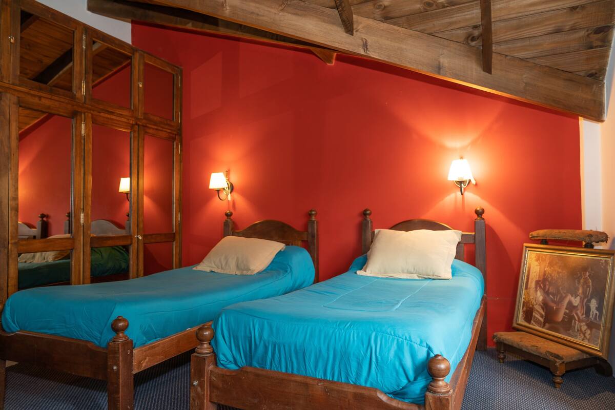 Une pièce avec deux lits en bois, des murs rouges et deux lampes fixées au mur.