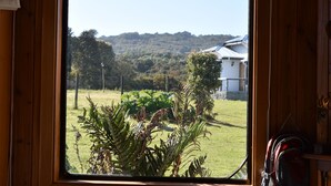 A window view of a grassy area with a house and trees in the background. - Vista Tranquila Chiloe (Chonchi)