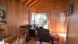 A cozy room with wooden walls and ceiling, a sofa, a dining table with chairs, and a view through a window. - Vista Tranquila Chiloe (Chonchi)