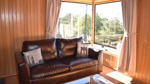 A brown leather sofa with a cushion featuring a cityscape design, positioned in a room with wooden walls and large windows. - Vista Tranquila Chiloe (Chonchi)