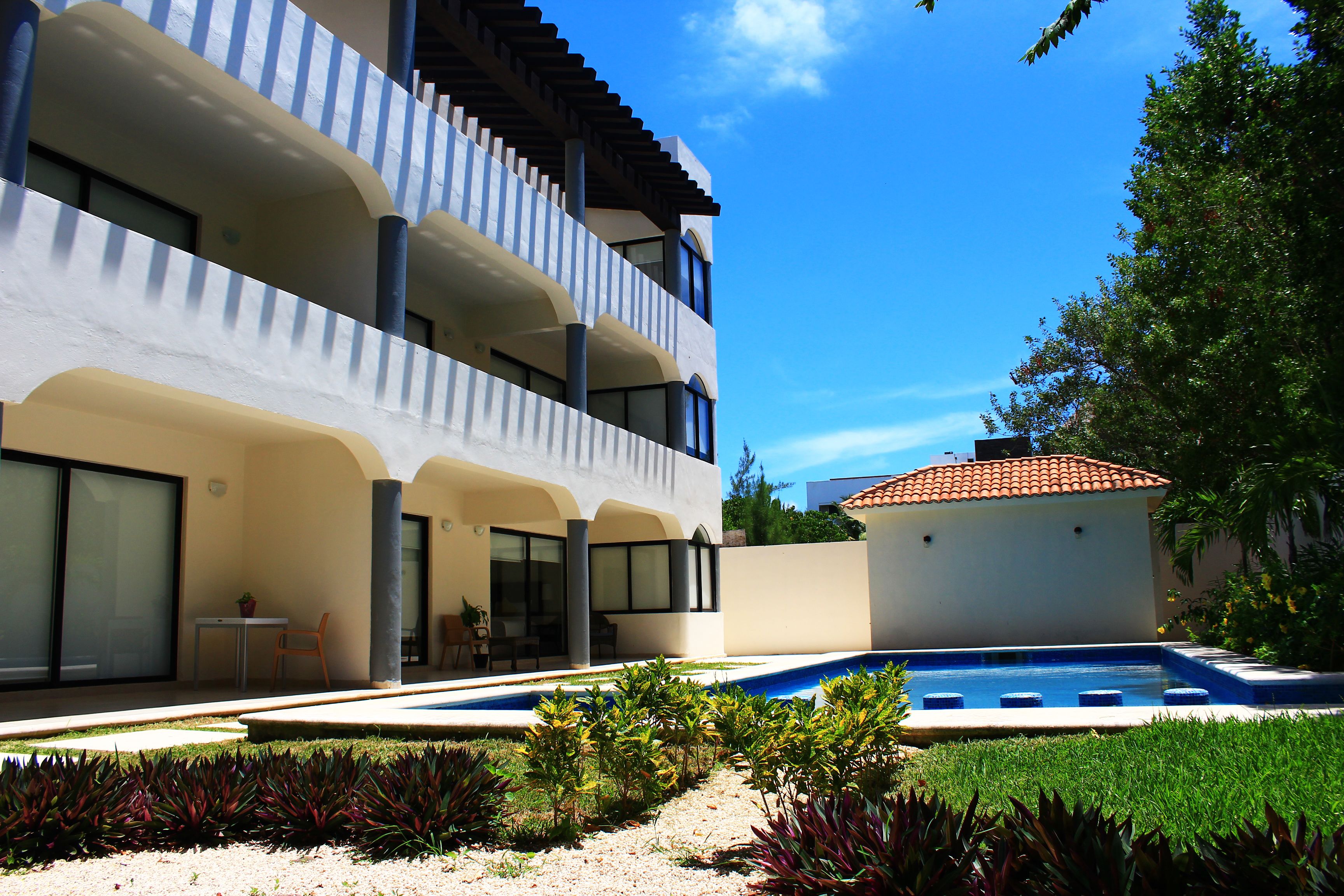 A modern two-story building with a swimming pool, outdoor seating, and a garden.