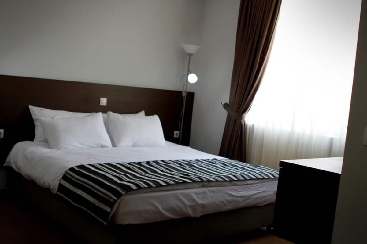 Una habitación de hotel con una cama, una lámpara de noche y un ventanal con cortinas.