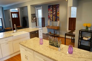 A modern kitchen with granite countertops, white cabinets, and a built-in dishwasher. There is a window with blinds, a wooden dining table, and a vase with flowers on a side table. - 3-Level Bucktown Home - Amazing Outdoors & Parking (Chicago)