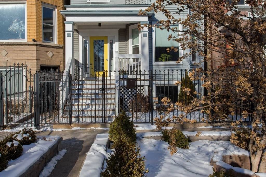 A residential building with a front porch, a yellow door, and a black metal fence.