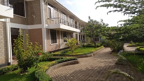 A multi-story building with a brick facade, a paved pathway, and well-maintained landscaping. - Kilimanjaro Eco Hostel (Moshi)