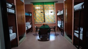 A dormitory room with bunk beds, a table with chairs, and a window with floral curtains. - Kilimanjaro Eco Hostel (Moshi)