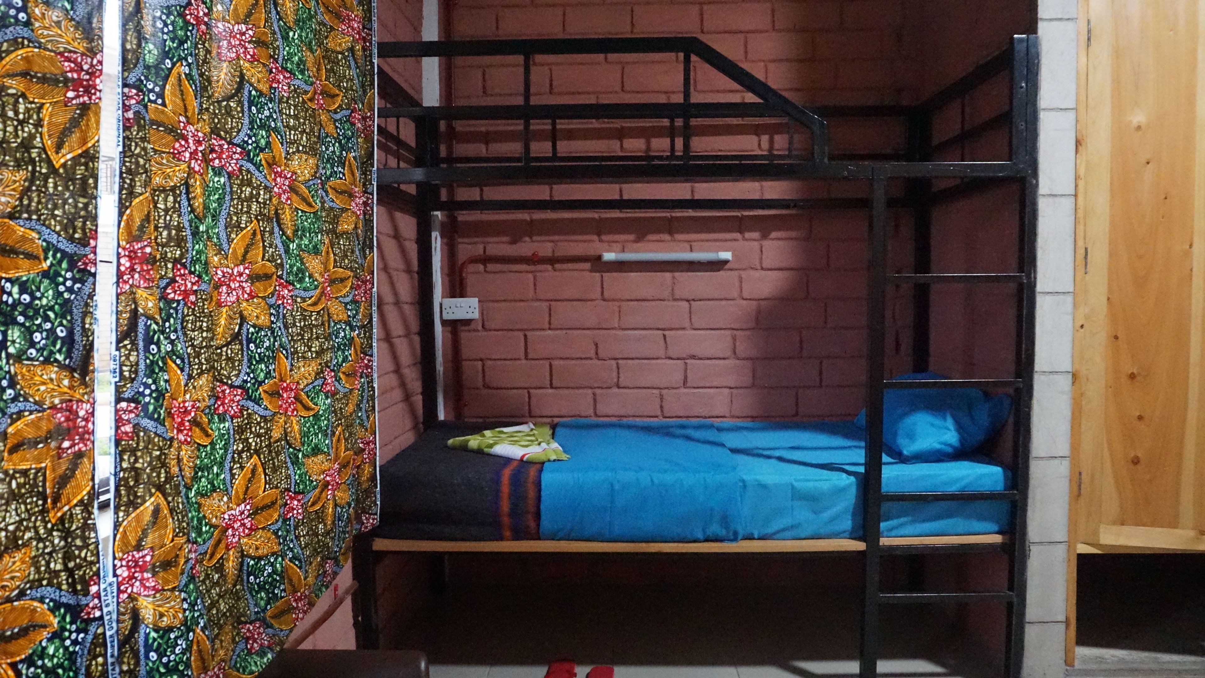 A bunk bed room with a brick wall, a window, and a colorful curtain.