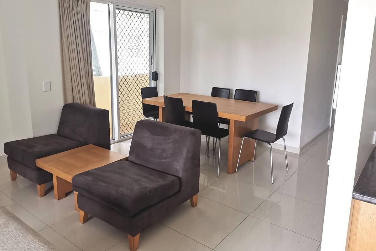 A modern living room with a sofa set, a dining table with chairs, and a sliding glass door leading to a balcony.