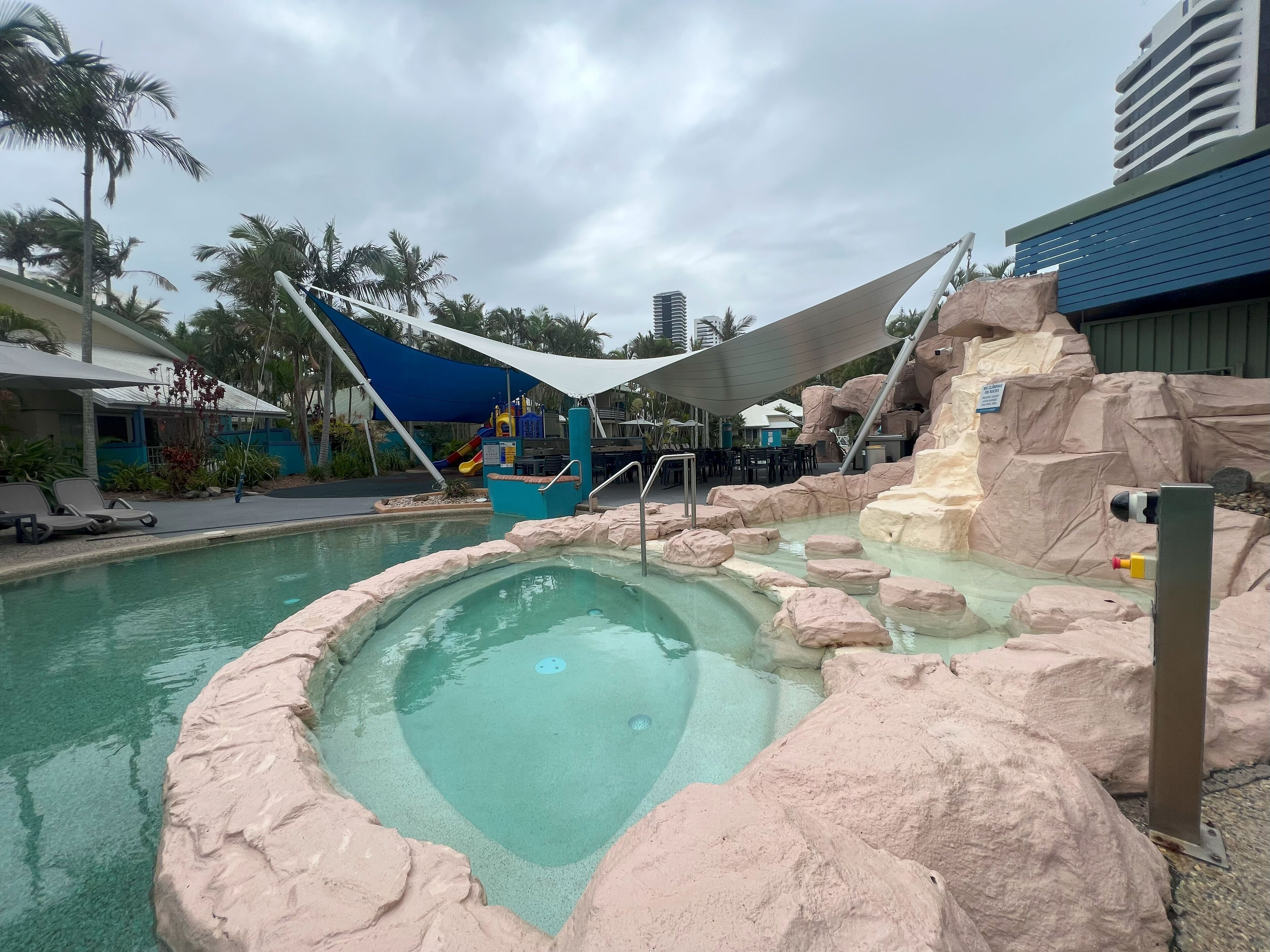 Area piscina con idromassaggio circondato da rocce artificiali, uno scivolo e sedie a sdraio.