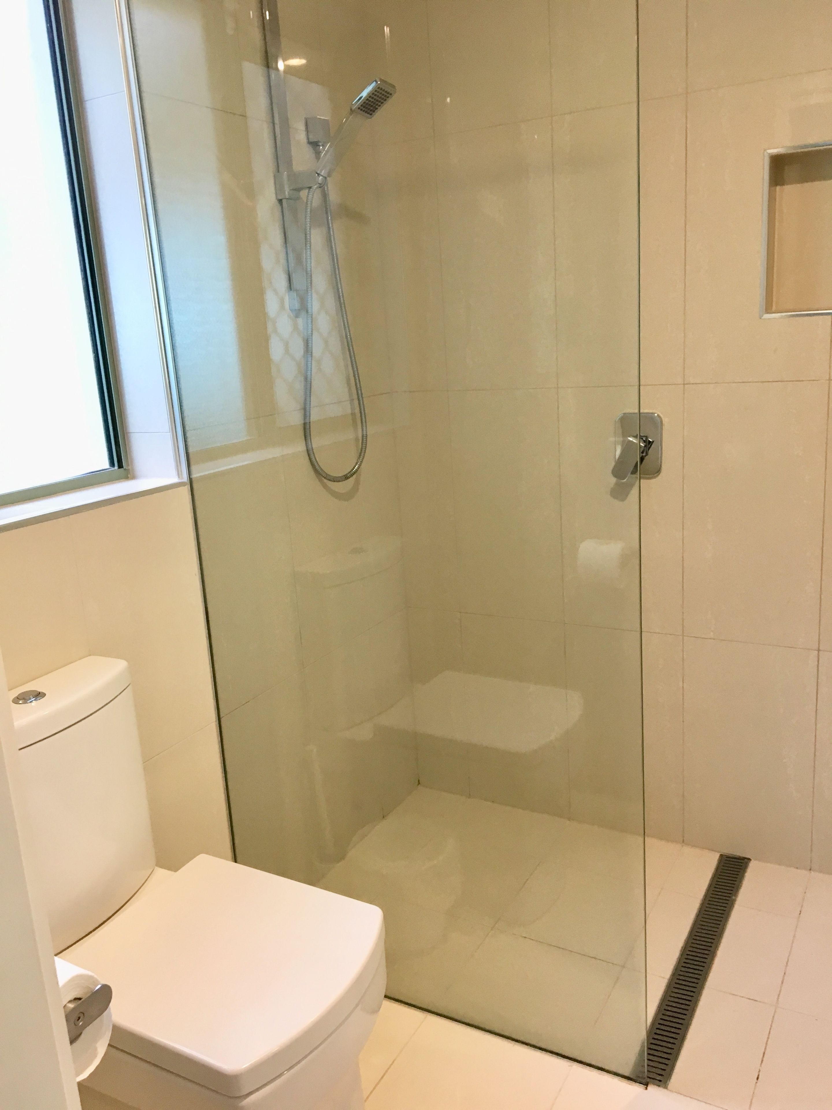 A modern bathroom with a glass-enclosed shower, a toilet, and a small window.
