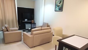 A living room with a beige sofa, a small table, and a TV stand. - Zahra Syariah Hotel (Kendari)