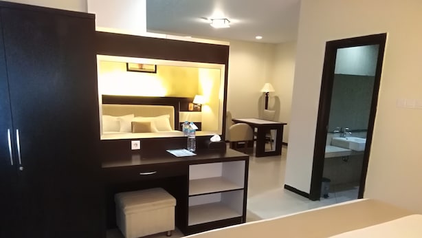 A hotel room with a bed, a desk with a chair, a mirror, a small table, and a wardrobe. - Zahra Syariah Hotel (Kendari)