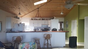 A kitchen with white cabinets, a wooden countertop, and a bar area with stools. There are ceiling fans and a window providing natural light. - Horizon House (Governor's Harbour)