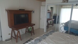 A bedroom with a bed, a television on a wooden stand, a wardrobe, and a door leading to another room. - Horizon House (Governor's Harbour)