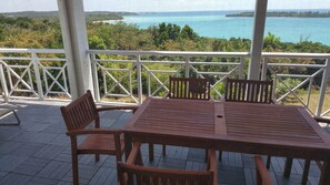 A wooden deck with a table and chairs, overlooking a coastal landscape with trees and a body of water. - Horizon House (Governor's Harbour)
