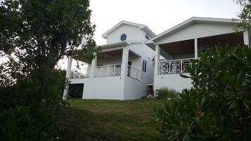 A two-story white house with a balcony, surrounded by greenery.