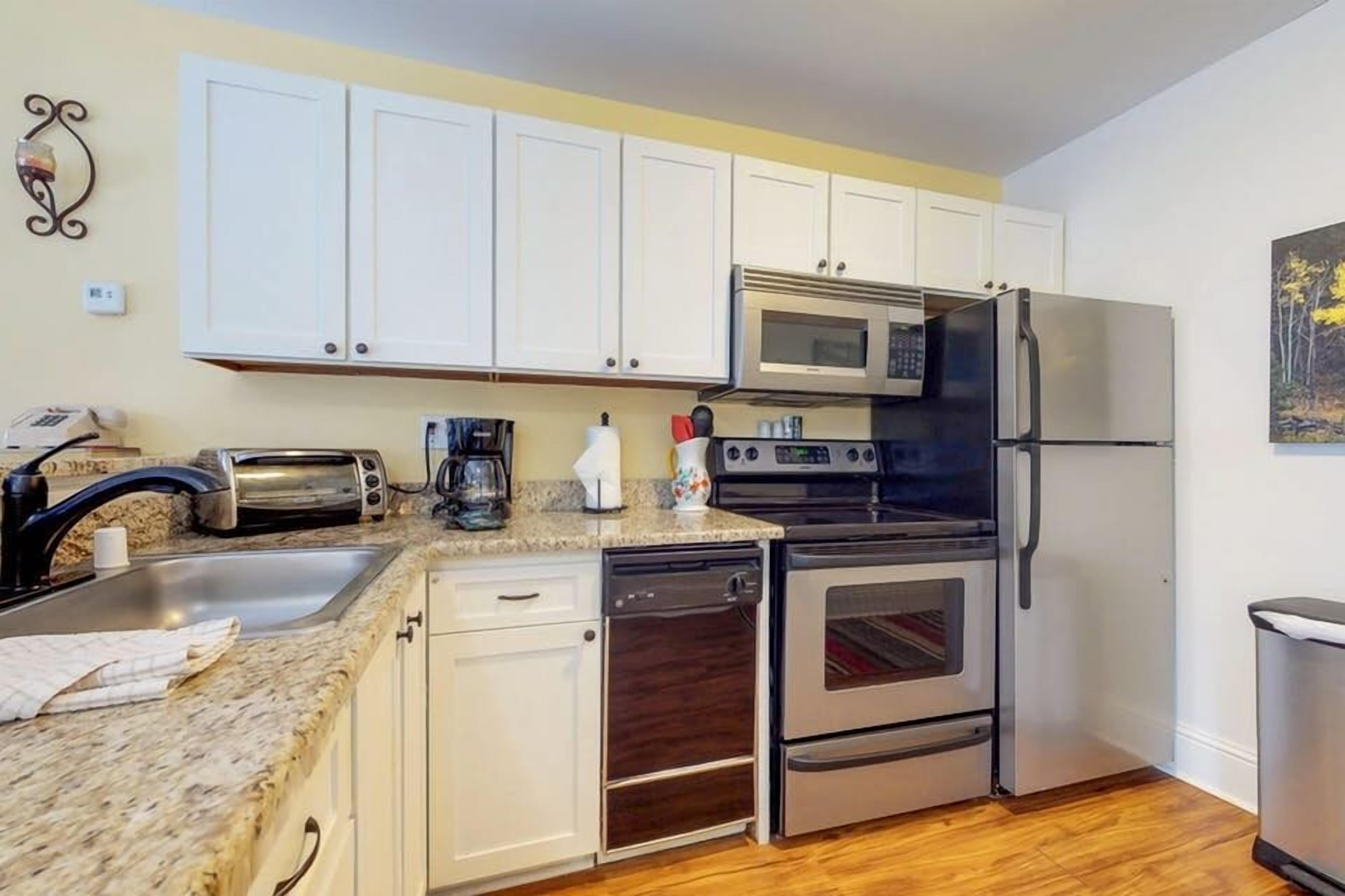 Una cocina compacta con armarios blancos, un refrigerador de acero inoxidable, un microondas, un tostador y un lavavajillas.
