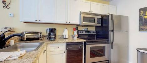 Una cocina compacta con armarios blancos, un refrigerador de acero inoxidable, un microondas, un tostador y un lavavajillas.