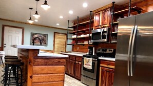 Une cuisine moderne dotée de meubles en bois, d’appareils électroménagers en acier inoxydable et d’un îlot central agrémenté de tabourets de bar.