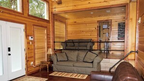 L’intérieur d’un chalet accueillant, avec un décor en bois, un canapé, un divan à motifs et une petite table surmontée d’une lampe.