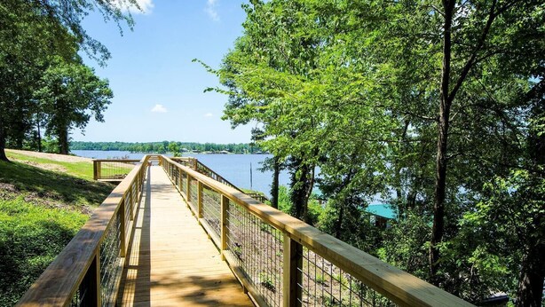 Une promenade en bois qui mène à un lac, entouré d’arbres et bordé d’un ciel dégagé.