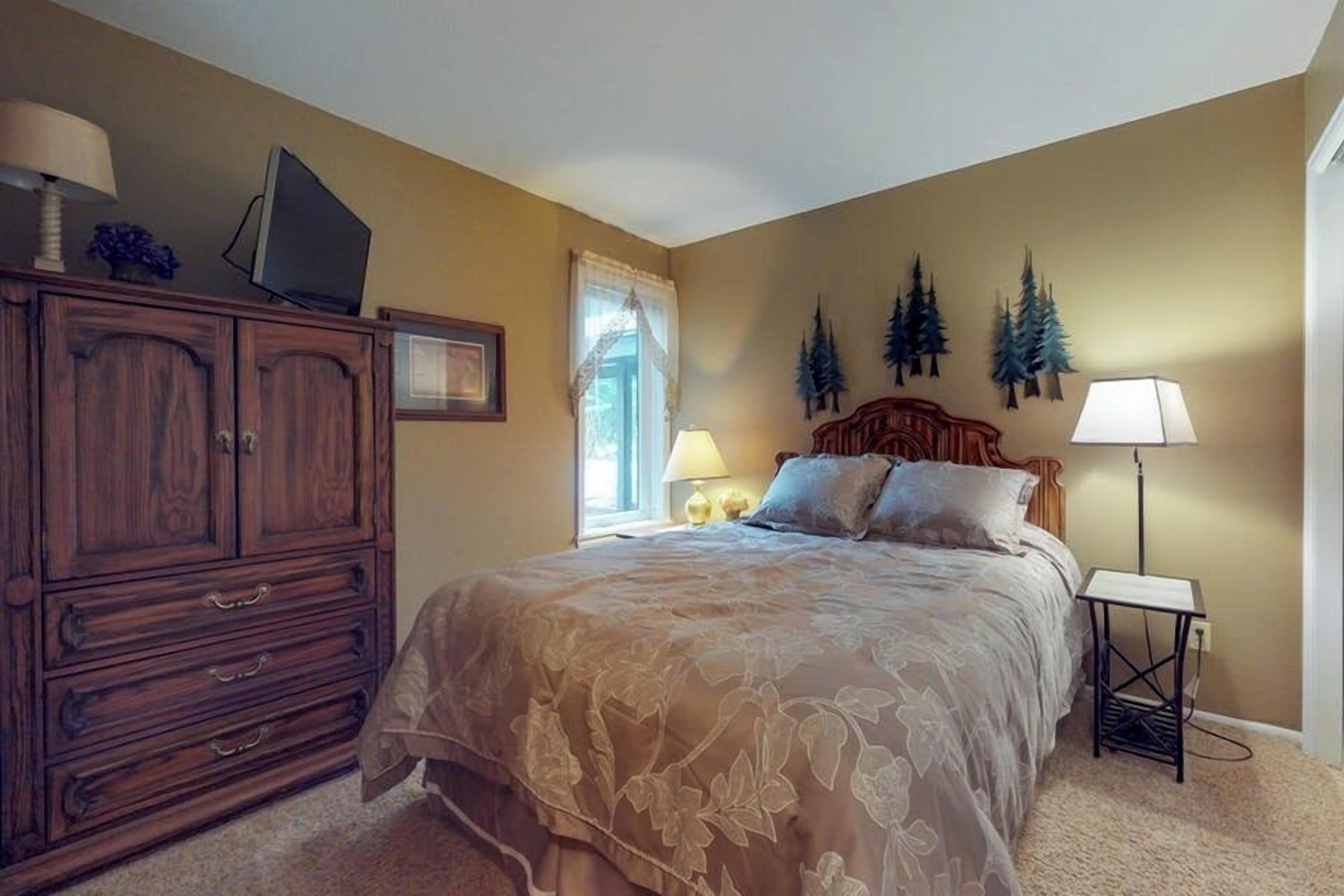 A bedroom with a bed, a dresser, a television on top of the dresser, and a lamp on the side.