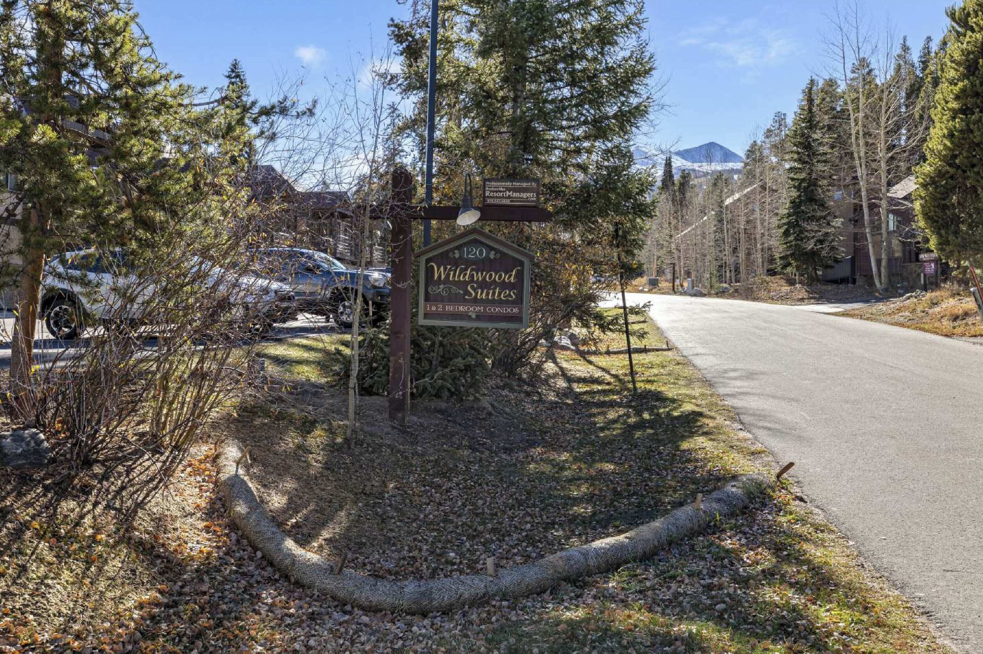 Schild für Wildwood Suites mit 1–2 Schlafzimmer-Wohnungen, umgeben von Bäumen und einer Straße.