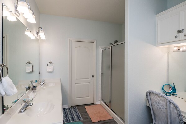 Une salle de bain avec un lavabo blanc, un miroir et un porte-serviettes. On y trouve également une douche avec une porte en verre et un meuble-lavabo avec un miroir et une serviette bleue.