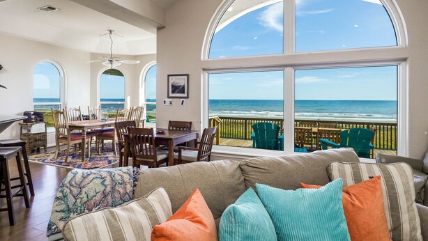 A spacious living area with a large window overlooking the ocean, a dining area with a view, and a cozy seating area with colorful cushions. - 1st row 4 bedroom 3 bath - Best views! (Galveston)