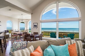 Een ruime woonkamer met een groot raam met uitzicht op de oceaan, een eethoek met panorama en een gezellige zithoek met kleurrijke kussens.
