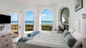 A bedroom with a large bed, a TV, and a view of the beach through arched windows. - 1st row 4 bedroom 3 bath - Best views! (Galveston)