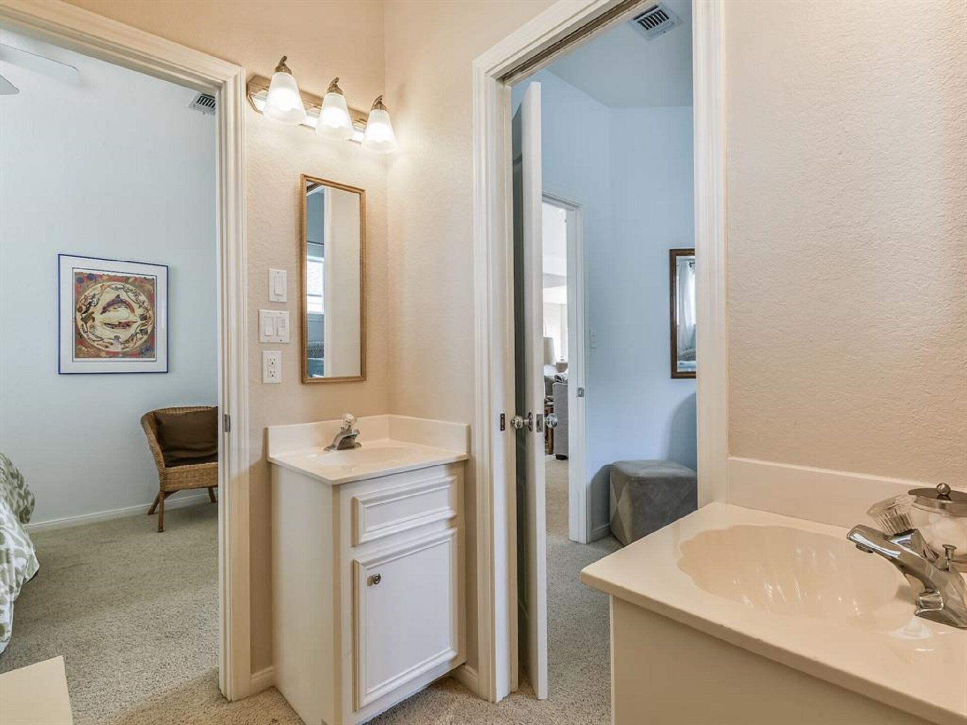 A bathroom with a white vanity, a sink, and a mirror. There is a framed picture on the wall and a chair in the corner.