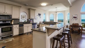 A spacious kitchen with a large island, stainless steel appliances, and a view of the ocean through arched windows. - 1st row 4 bedroom 3 bath - Best views! (Galveston)