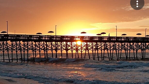 A pier extending into the water with the sun setting in the background.