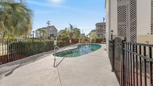 A swimming pool with a metal fence, surrounded by buildings and palm trees.
