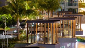 A modern hotel with a glass-enclosed outdoor lounge area, palm trees, and a pool. - Queens Suite by D Imperio Homestay (George Town)