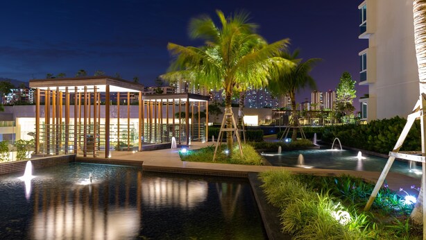 A nighttime view of a hotel pool area with a water fountain, palm trees, and a modern building structure. - Queens Suite by D Imperio Homestay (George Town)