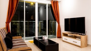 A modern living room with a sofa, a black coffee table, a wooden TV stand, and a sliding glass door with curtains. - Queens Suite by D Imperio Homestay (George Town)