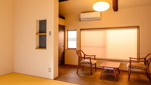A room with a wooden floor, a large window with blinds, two chairs, a small table, and a wall-mounted air conditioner. - Koume no Hanare (Kyoto)